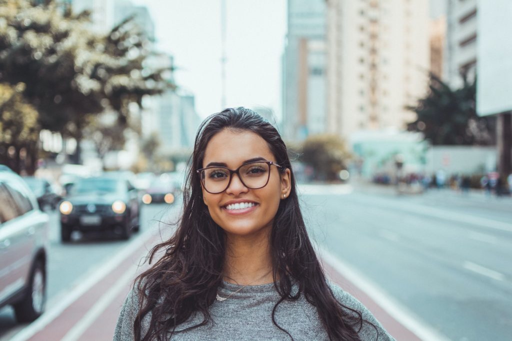 Young woman with glasses smiling at camera in street